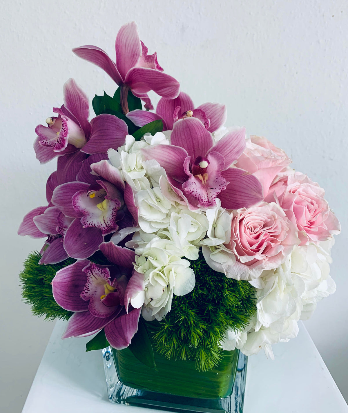 Natural Bliss arrangement of white hydrangea, dusty pink cymbidium and blush roses in a square glass vase