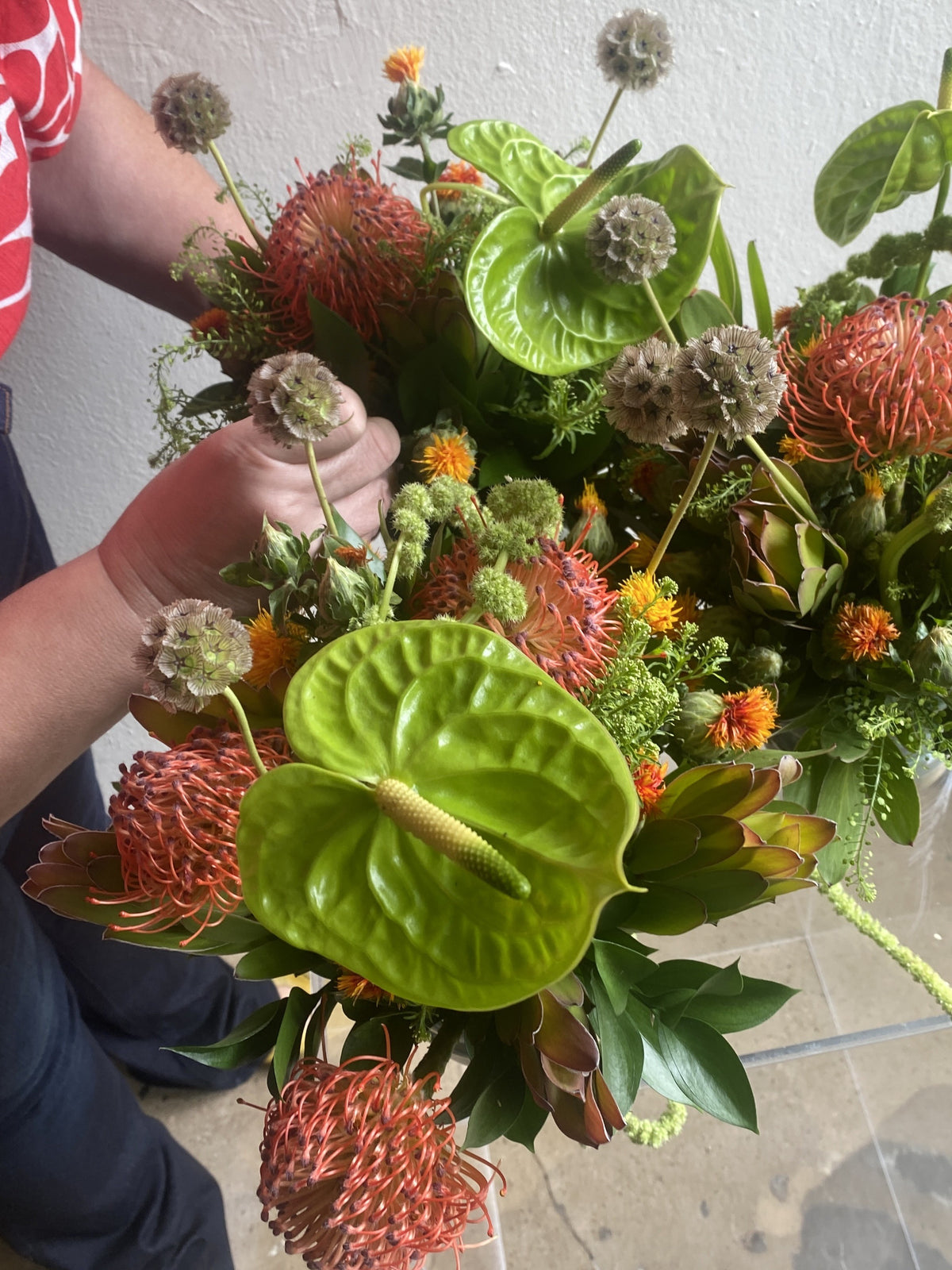 Teremar Pumarada holding a finished arrangement of green anthuriums and orange pincushion proteas