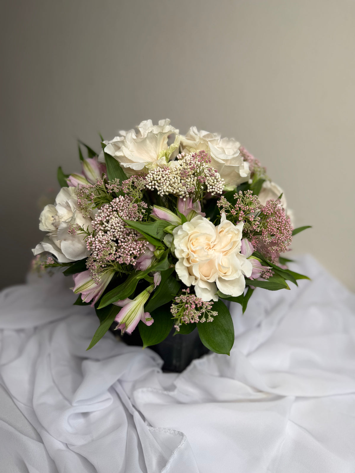 Ethereal arrangement of ivory blooms and blush accents set in lush greenery