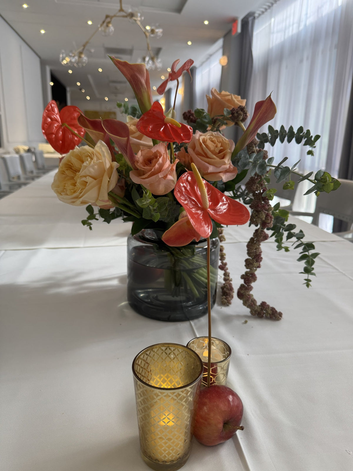 Anthurium, peach roses and eucalyptus with gold votives and red apples