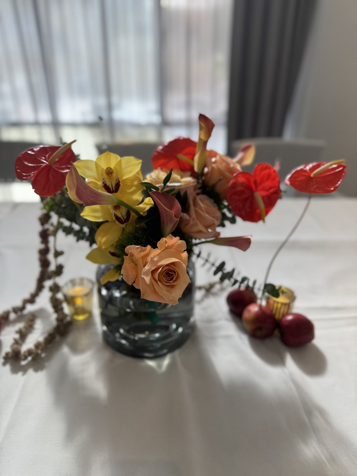 Yellow orchid, peach roses and red anthurium in a smoked glass vase
