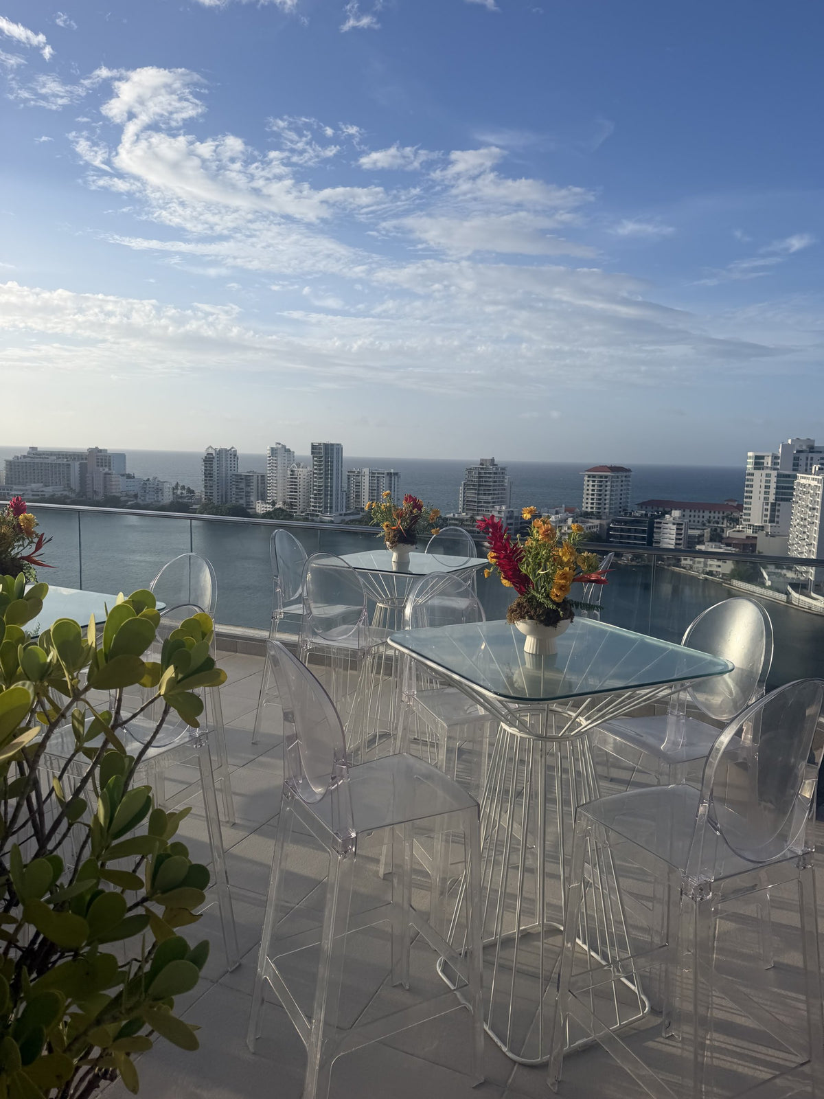 Terrace with clear chairs and tropical arrangements, the San Juan skyline and the sea behind