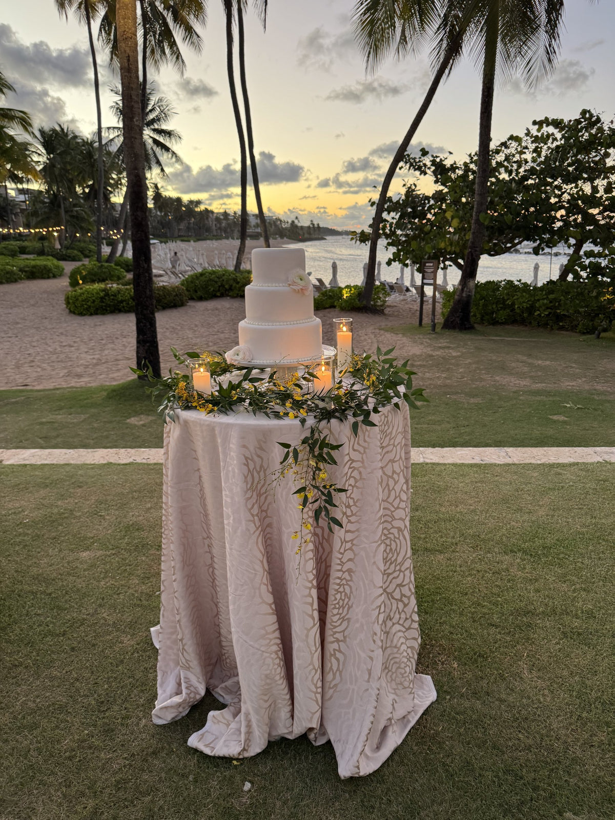 Wedding cake with a eucalyptus garland, palm trees and the sea at sunset in Dorado