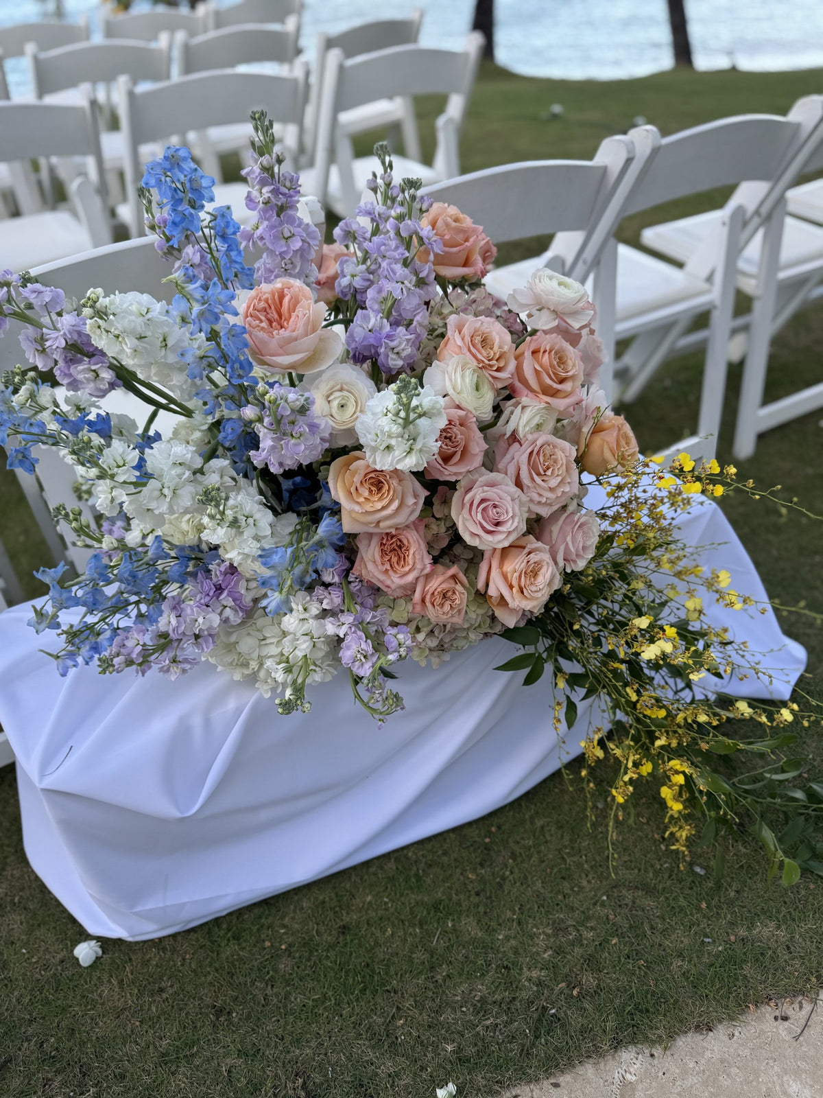 Ceremony aisle arrangement of peach roses, delphinium and yellow oncidium