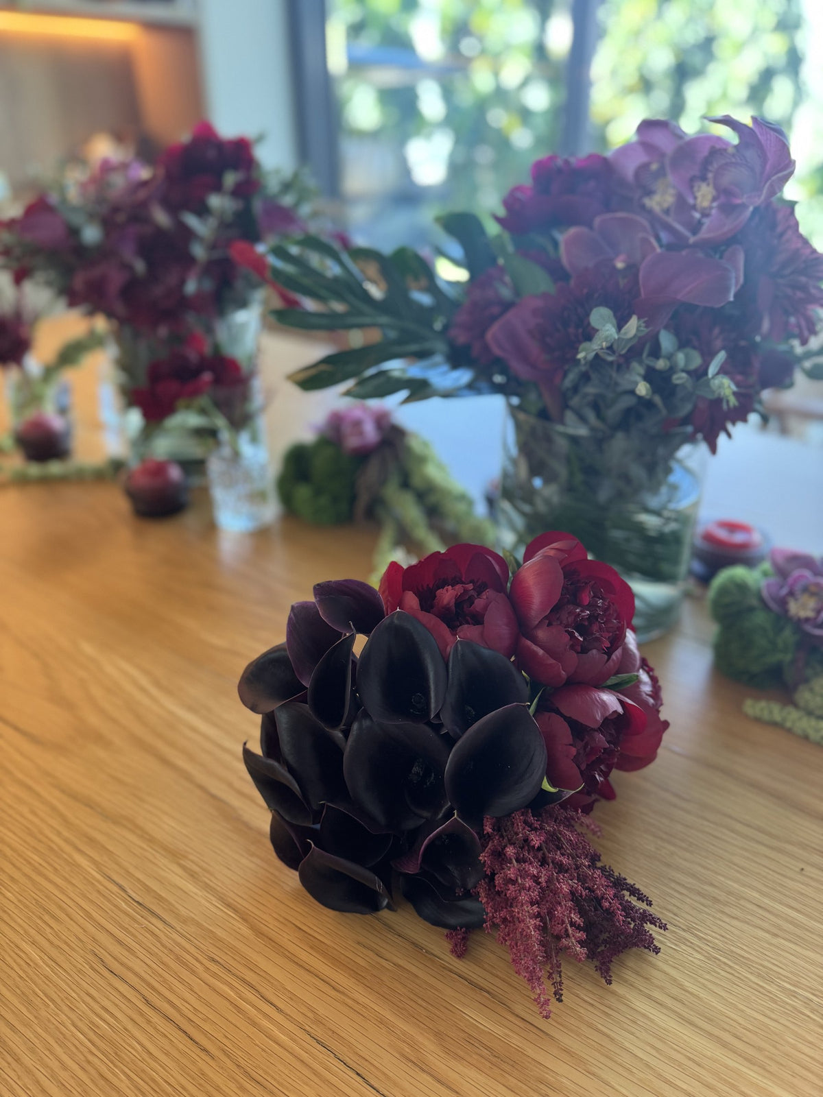 Black calla lilies and red peonies beside a tall burgundy arrangement