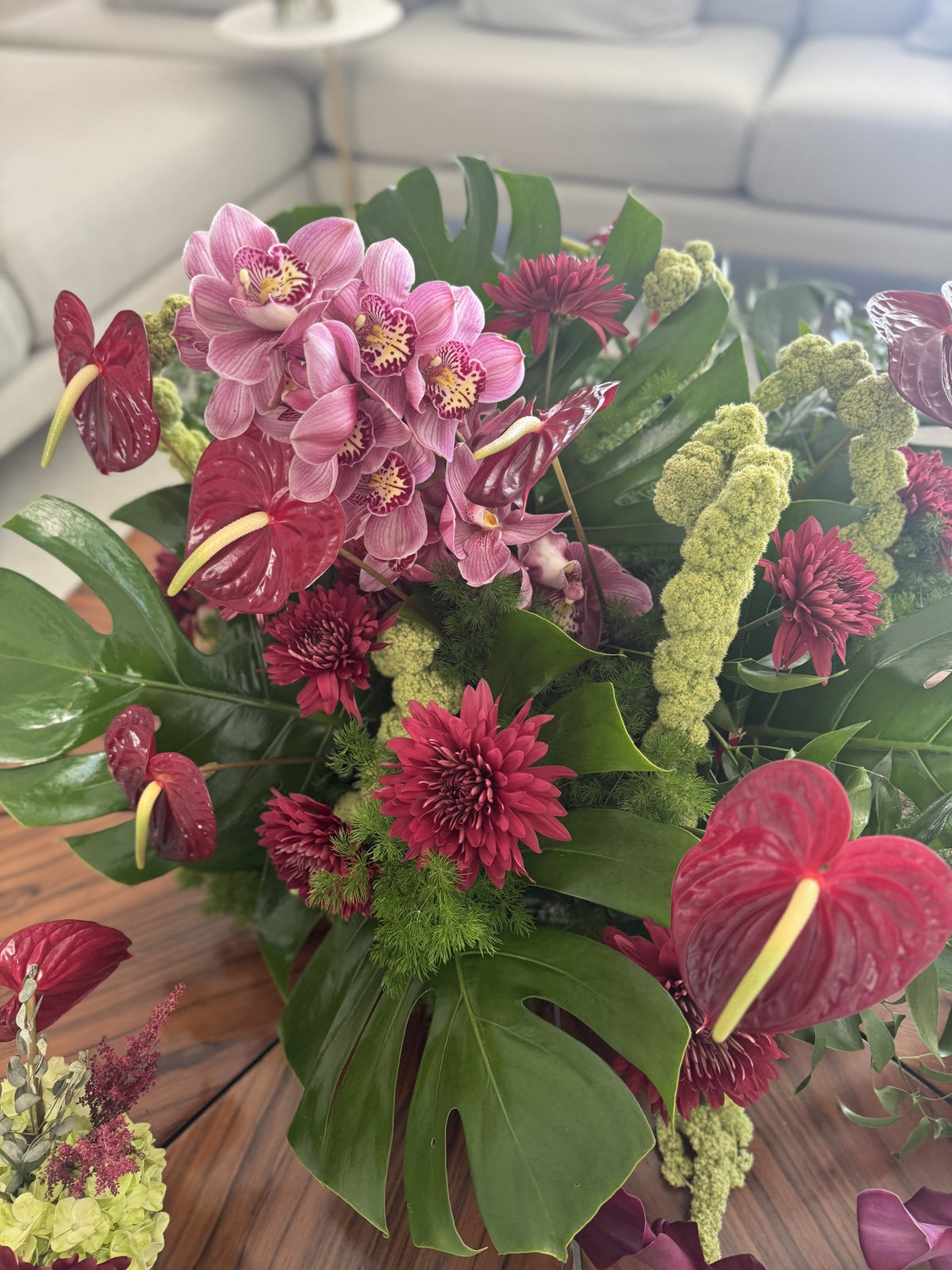 Pink cymbidium orchids, red anthurium and monstera leaves in a low arrangement