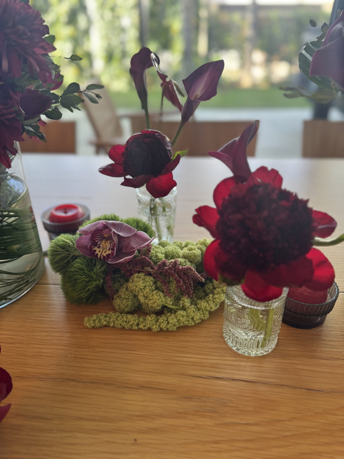 Red peony and burgundy calla lily in bud vases with moss on a wooden table