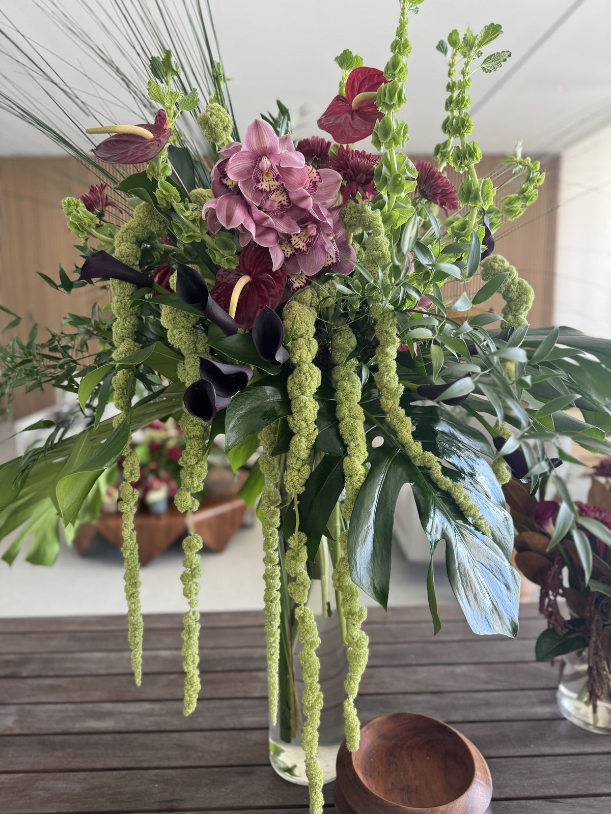 Tall arrangement of pink cymbidium, bells of Ireland, monstera and hanging amaranth