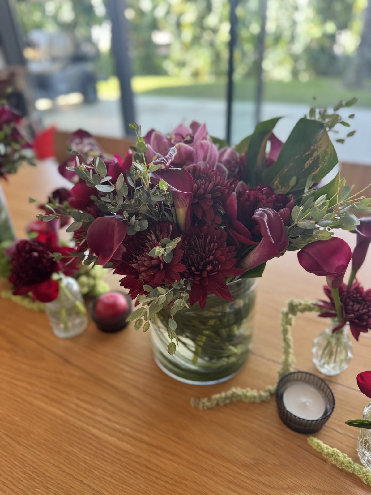 Burgundy roses, anthurium and eucalyptus in a glass vase with candles