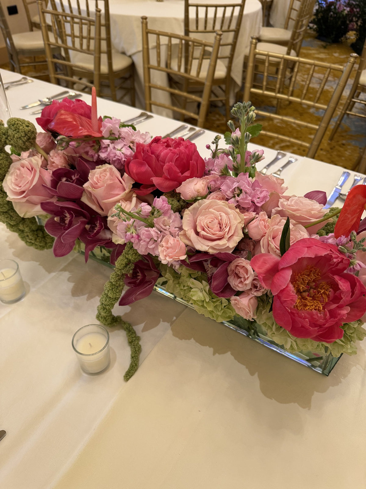 Low arrangement of coral peonies, pink roses, stock and orchids with candles