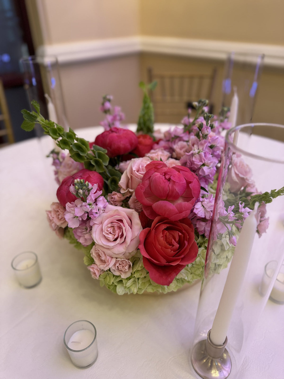 Gold bowl centerpiece of coral peonies, red roses and pink stock with taper candles
