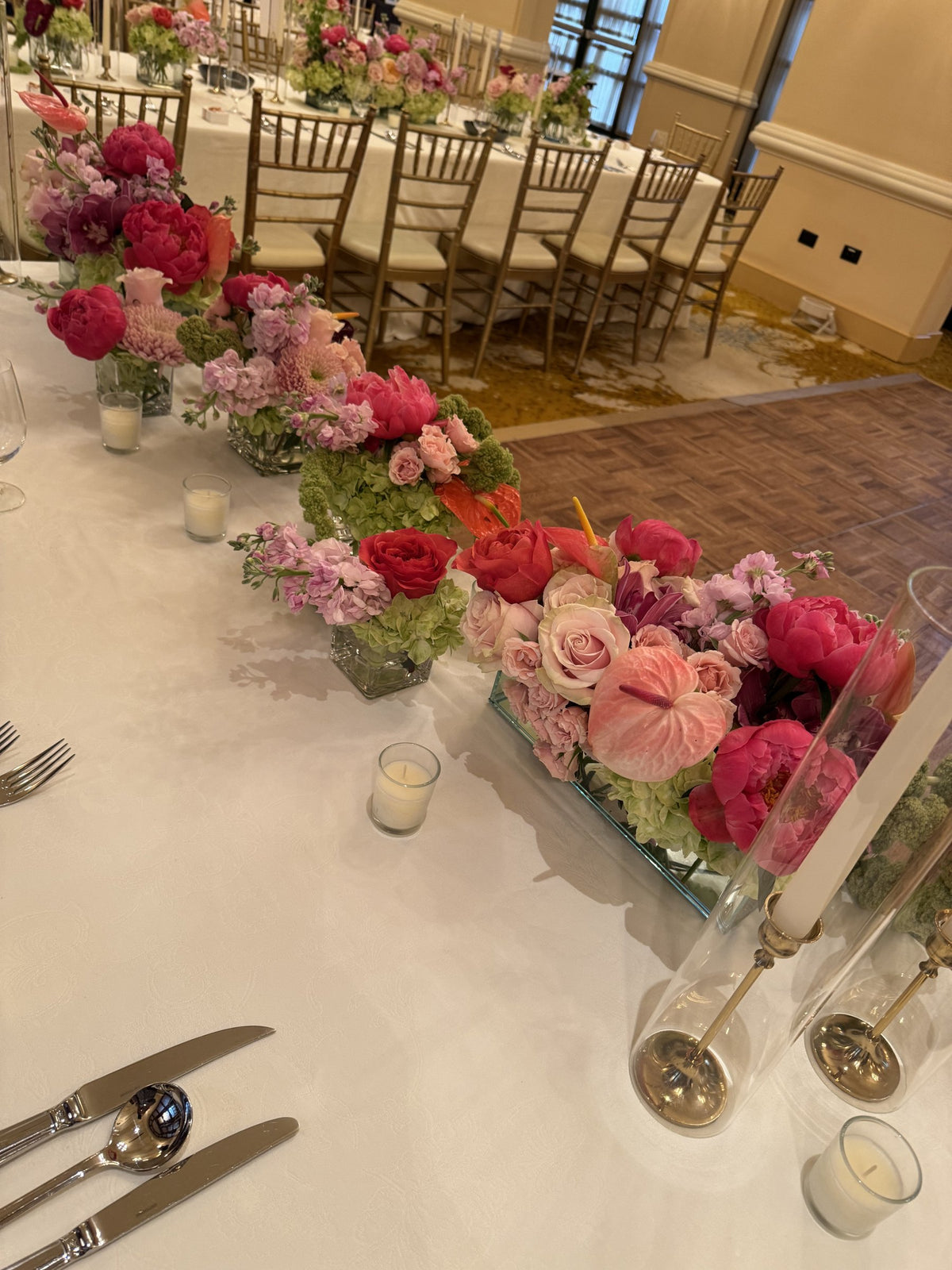 Long banquet table with a runner of coral peonies, roses and hydrangea, gold chairs