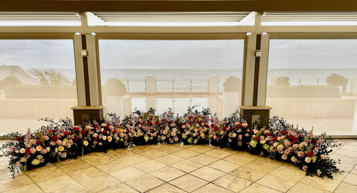 Floral arch of pink and coral flowers across a terrace overlooking the sea