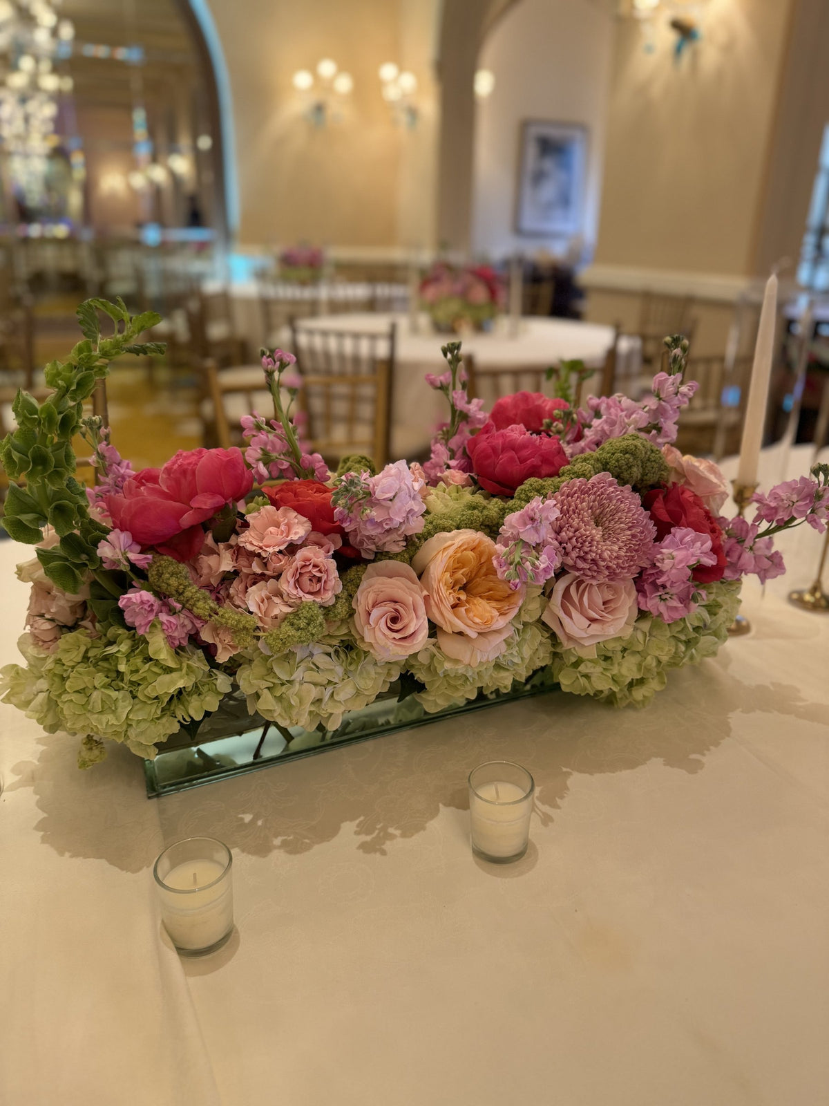Low centerpiece of garden roses, dahlias, peonies and hydrangea in a ballroom