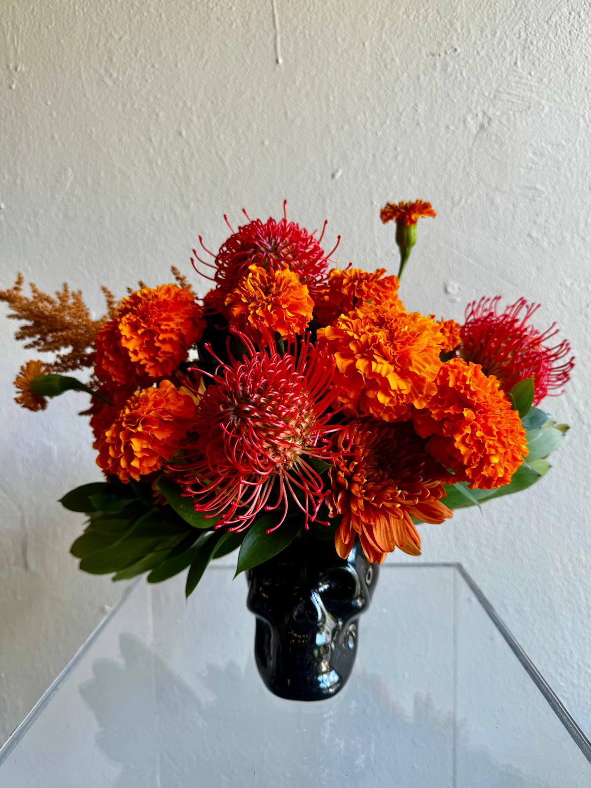 Arreglo de Halloween en una calavera negra con cempasúchil naranja y protea roja