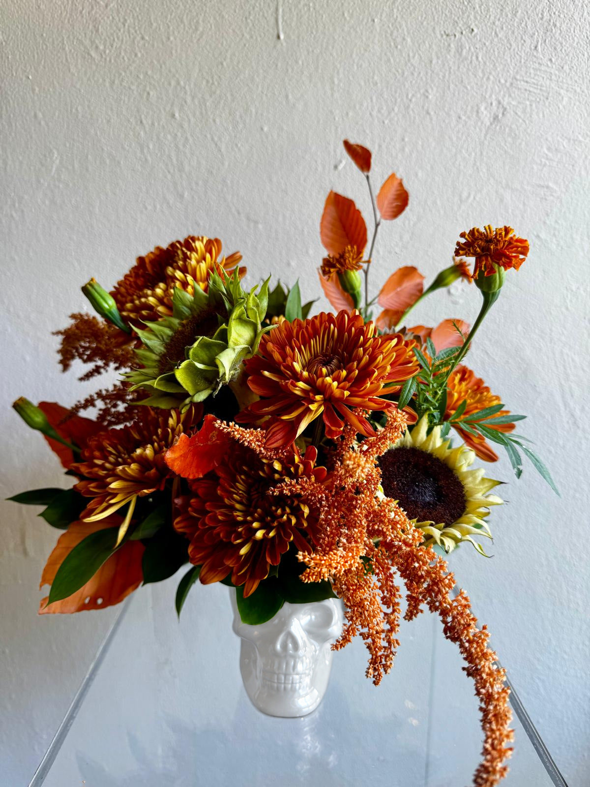 Halloween arrangement in a white skull with sunflowers, copper chrysanthemums and orange marigolds