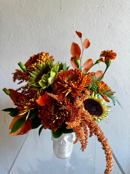 Halloween arrangement in a white skull with sunflowers, copper chrysanthemums and orange marigolds