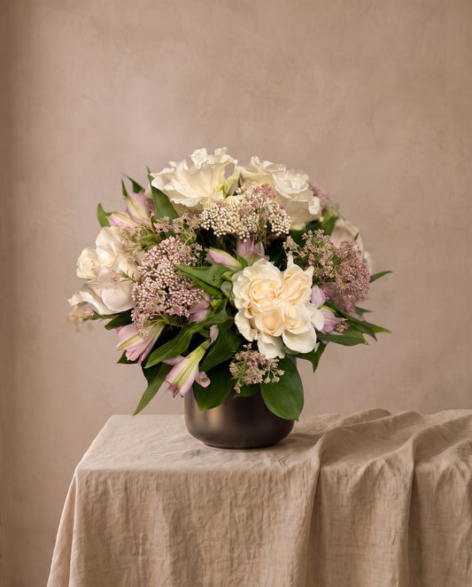 Ethereal arrangement of ivory blooms and blush accents set in lush greenery