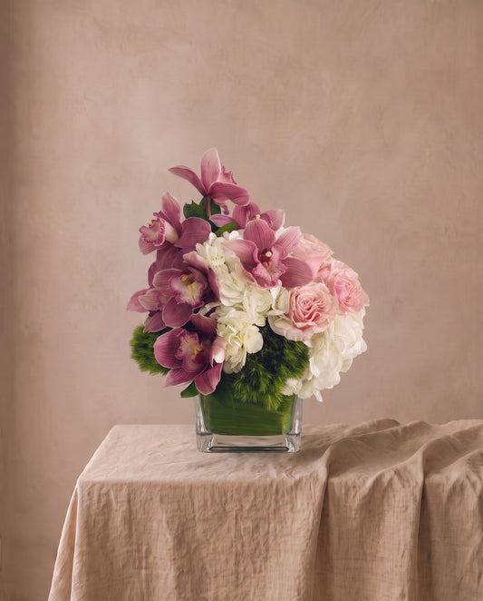 Natural Bliss arrangement of white hydrangea, dusty pink cymbidium and blush roses in a square glass vase