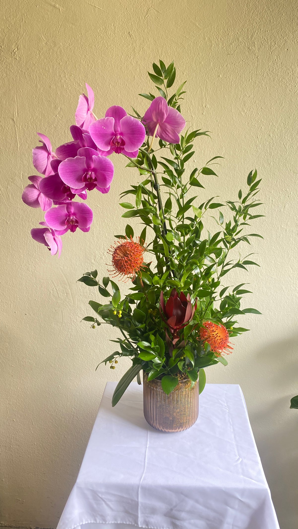 Single Phalaenopsis orchid arrangement with pincushion proteas and ruscus in a ribbed glass vase