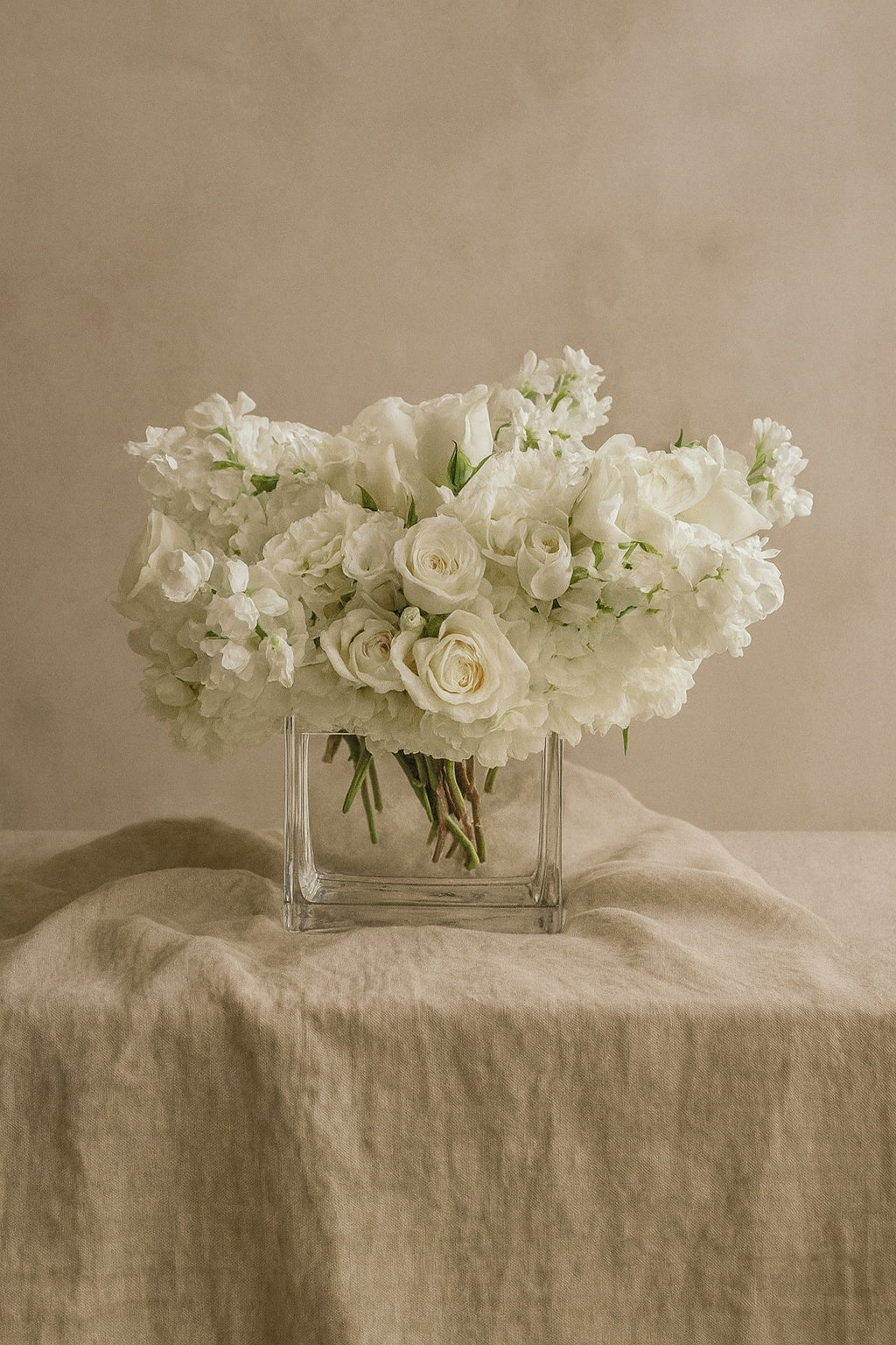 White Blooms arrangement of white hydrangea, spray roses and stock in a square crystal vase